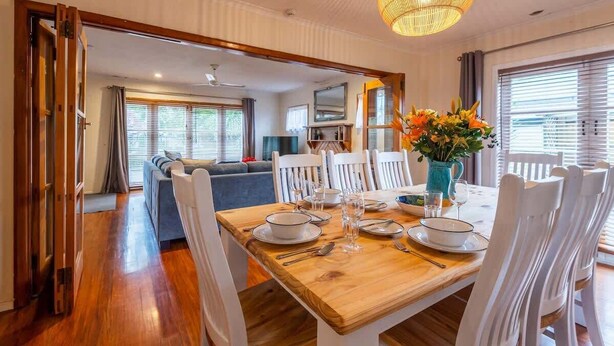 Un comedor con una mesa de madera preparada para cuatro personas, sillas blancas y un florero con flores.