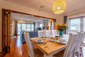 Un comedor con una mesa de madera dispuesta para cuatro personas, sillas blancas y un florero con flores.