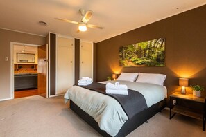 Un dormitorio con cama, mesitas de noche, ventilador de techo, un cuadro y un armario.