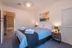 Un dormitorio con cama, mesitas de noche, un cuadro y una puerta.