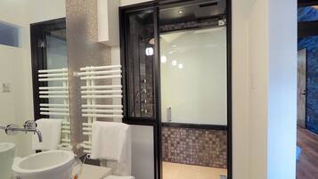 Une salle de bain moderne avec un grand miroir, un lavabo blanc et un espace douche doté d’une porte en verre.