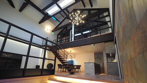 A modern interior with a staircase leading to a second floor, a dining area with a table and chairs, and a kitchen area. - Pres De La Mer (Hakodate)