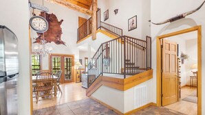 Un interior espacioso con una escalera de madera, un comedor y un gran reloj.