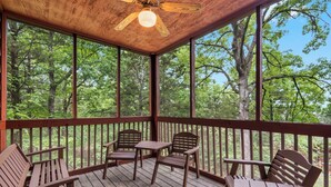 Una terraza de madera con cuatro sillas y una mesa, con vista a un área boscosa.