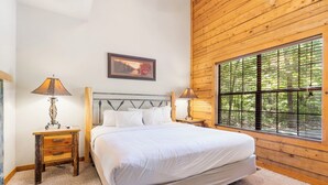 A bedroom with a large bed, wooden walls, a window with blinds, and two bedside tables with lamps. - Roomy 2BR+Loft Walk-in Cabin near Shows, Shopping, and Dining! (Branson)