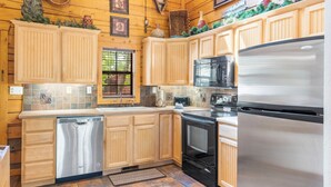 A kitchen with wooden cabinets, stainless steel appliances, and a window with a view of greenery. - Roomy 2BR+Loft Walk-in Cabin near Shows, Shopping, and Dining! (Branson)