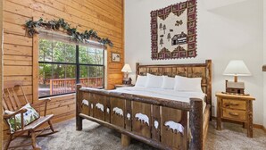 Een houten kamer in chaletstijl met een bed, schommelstoel en een raam met uitzicht op bomen.