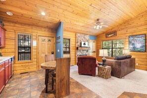 Cozy cabin interior with a seating area, kitchen, and large window.