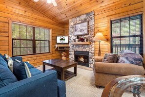 A cozy cabin interior with a stone fireplace, wooden walls, a blue sofa, and a television.