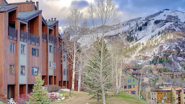A multi-story wooden building with balconies, a ski resort in the background, and a mountainous landscape. - Steps to Mtn/Resort/Free Town Bus (Across St)+ Heated Pool-HotTub-Grill-Updated-Spacious-2 Levels (Steamboat Springs)