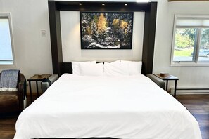 A bedroom with a large bed, a painting of a forest scene, and two windows. - Steps to Ski/Town Bus/Pool/HotTub/Grill-2 Levels (Steamboat Springs)