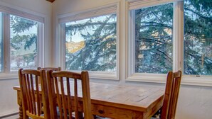 A dining area with a wooden table and chairs, large windows with a view of snow-covered trees. - Steps to Mtn/Resort/Free Town Bus (Across St)+ Heated Pool-HotTub-Grill-Updated-Spacious-2 Levels (Steamboat Springs)