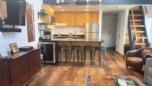A compact kitchen with wooden cabinets, a stainless steel refrigerator, and a bar stool area. - Steps to Mtn/Resort/Free Town Bus (Across St)+ Heated Pool-HotTub-Grill-Updated-Spacious-2 Levels (Steamboat Springs)