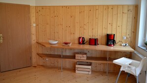 Une cuisine avec des murs en bois, un plan de travail en bois, un saladier blanc, une machine à café rouge et une chaise haute blanche.