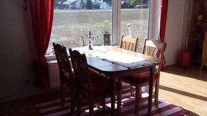 Un coin repas avec une table et des chaises, une vue sur les maisons à travers de grandes fenêtres et un tapis rayé rouge et blanc.