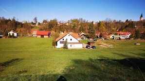 Un paysage rural avec une maison blanche, une grange à toit rouge et une église en arrière-plan.