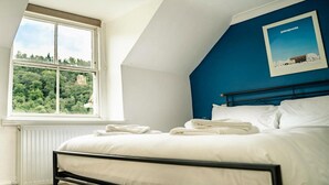A bedroom with a bed, a window with a view of greenery, and a blue accent wall. - Holiday Home in Ross on Wye Near Goodrich Castle (Ross-on-Wye)