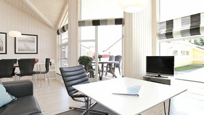 A modern living room with a white table, black leather chairs, a black sofa, and a flat-screen TV. - Holiday Home in Großenbrode (Grossenbrode)