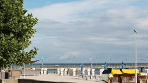 A beachside promenade with rows of beach chairs and umbrellas, a concrete walkway, and a view of the sea. - Holiday Home in Großenbrode (Grossenbrode)