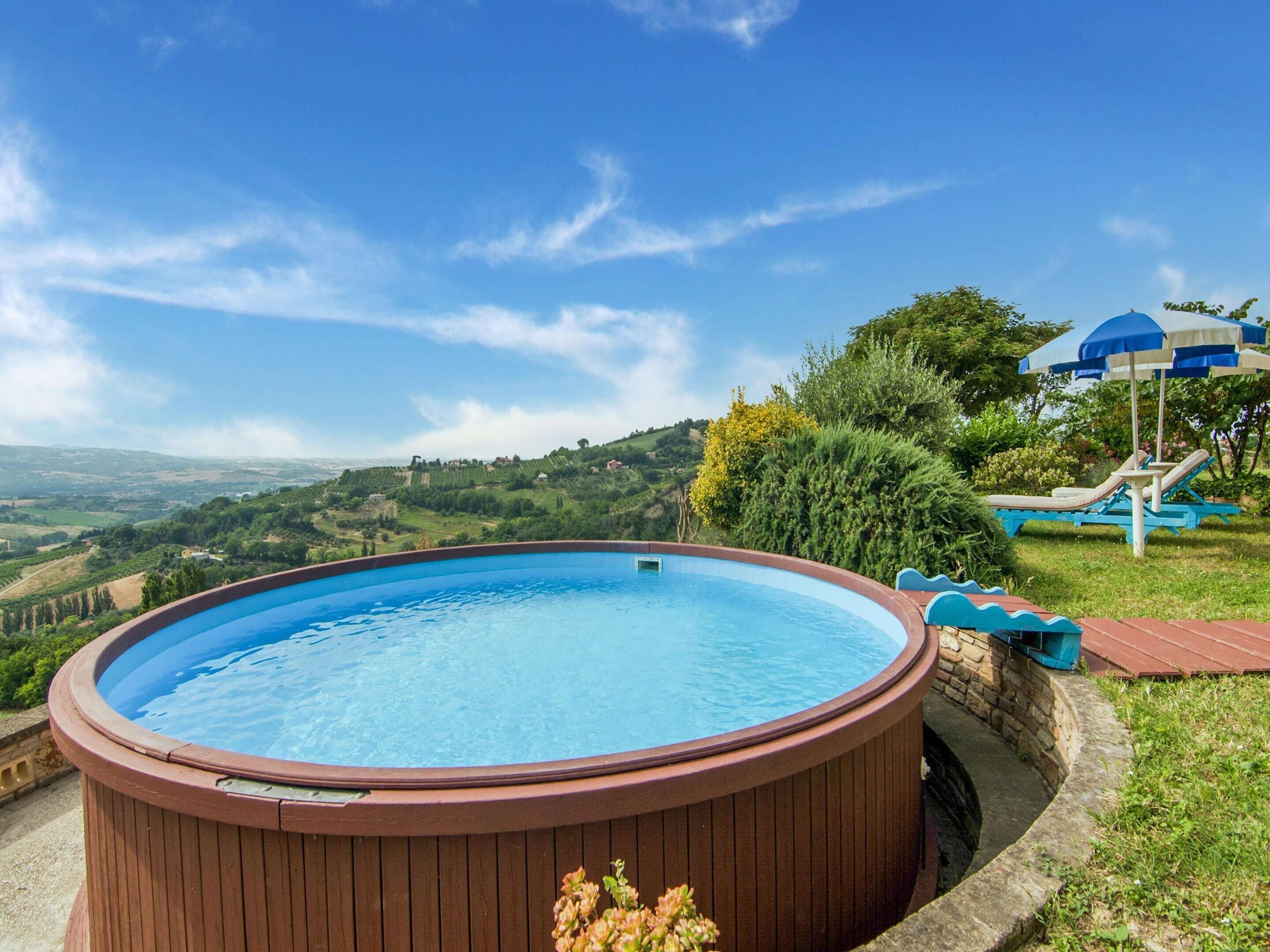 Een jacuzzi omringd door een stenen muur, met uitzicht op een weelderig landschap en een blauwe parasol op de achtergrond.