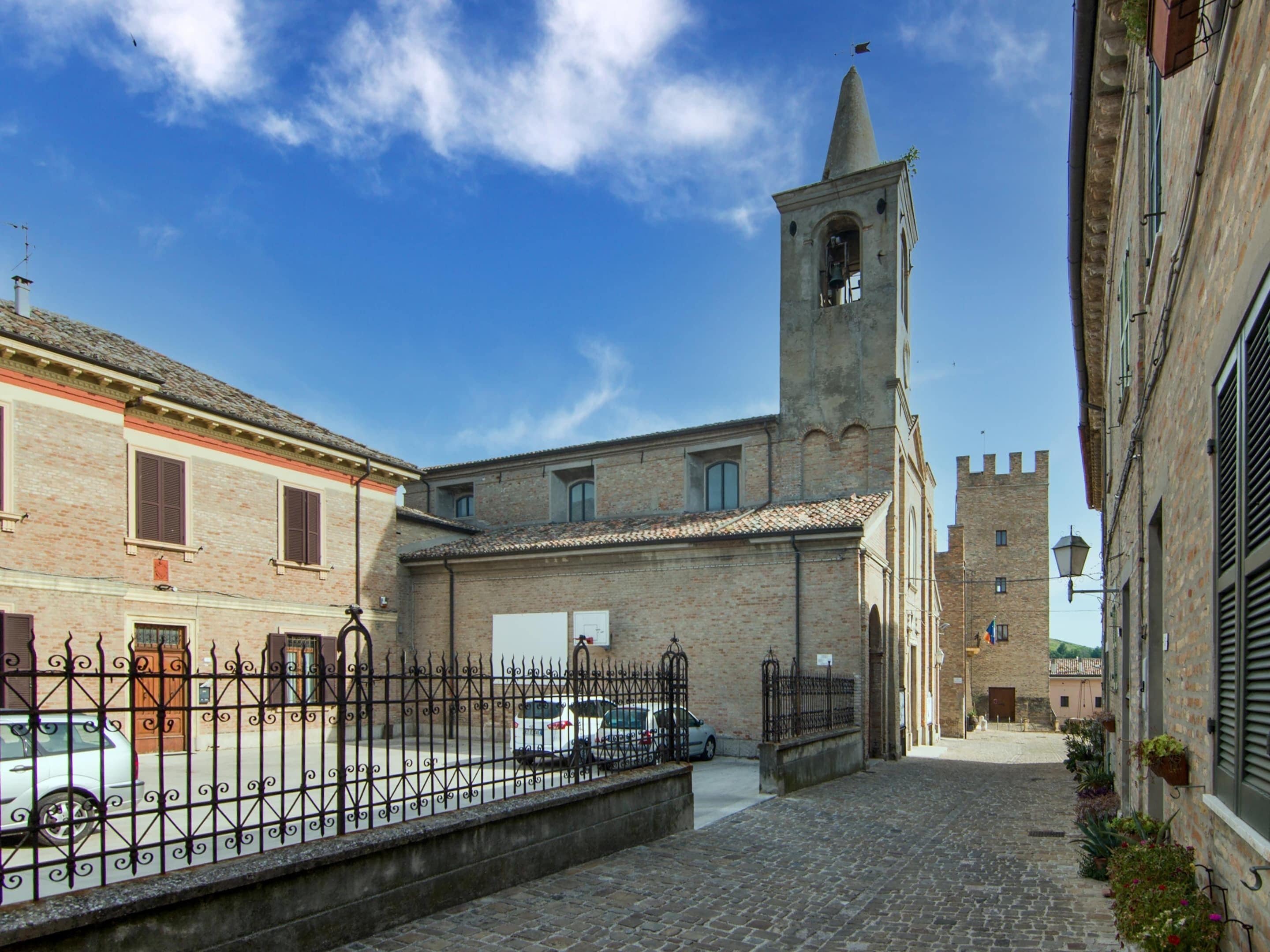 A narrow cobblestone street with a historic building featuring a bell tower and a stone tower in the background.