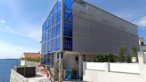 A modern building with a glass facade, a sign for 'APARTMAN', and a view of the sea. - Sea View Apartment in Okrug Gornji near Trogir Center (Okrug)