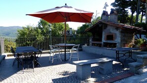An outdoor patio with a table and chairs, a red umbrella, and a stone barbecue area. - Holiday Home in Montecarelli With Pool (Barberino di Mugello)