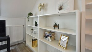 A white shelving unit with a cactus, a bicycle, books, and a framed picture. - Modern Holiday Home in Wolphaartsdijk With Private Garden (Wolphaartsdijk)