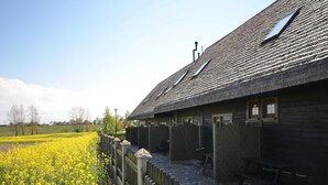 A traditional wooden building with a sloped roof, a fenced area with yellow flowers, and a stone bench. - Cozy Studio 1 at the Seaside Agrotourism (Darlowo)