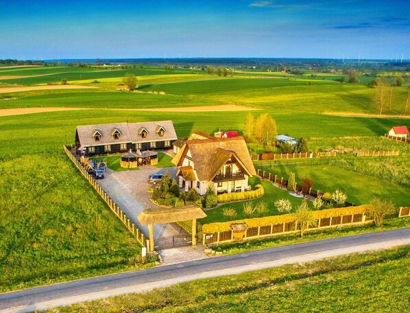A rural property with a main house, a smaller building, and a fenced area with a thatched-roof structure.