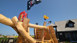 A wooden play structure with a pirate flag, a Minion figure, and a house in the background. - Cozy Studio 1 at the Seaside Agrotourism (Darlowo)