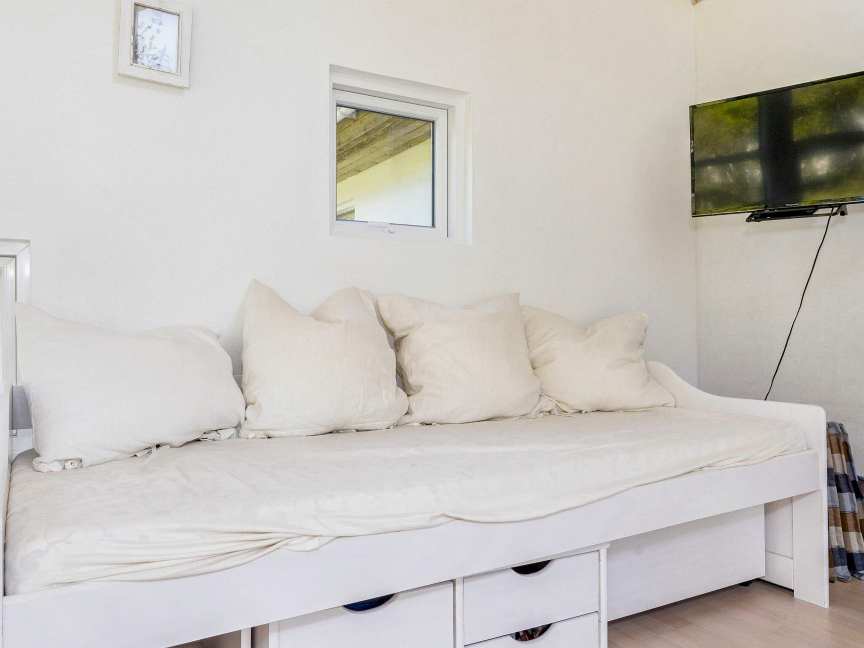 Uma cama branca com várias almofadas e uma televisão presa na parede.