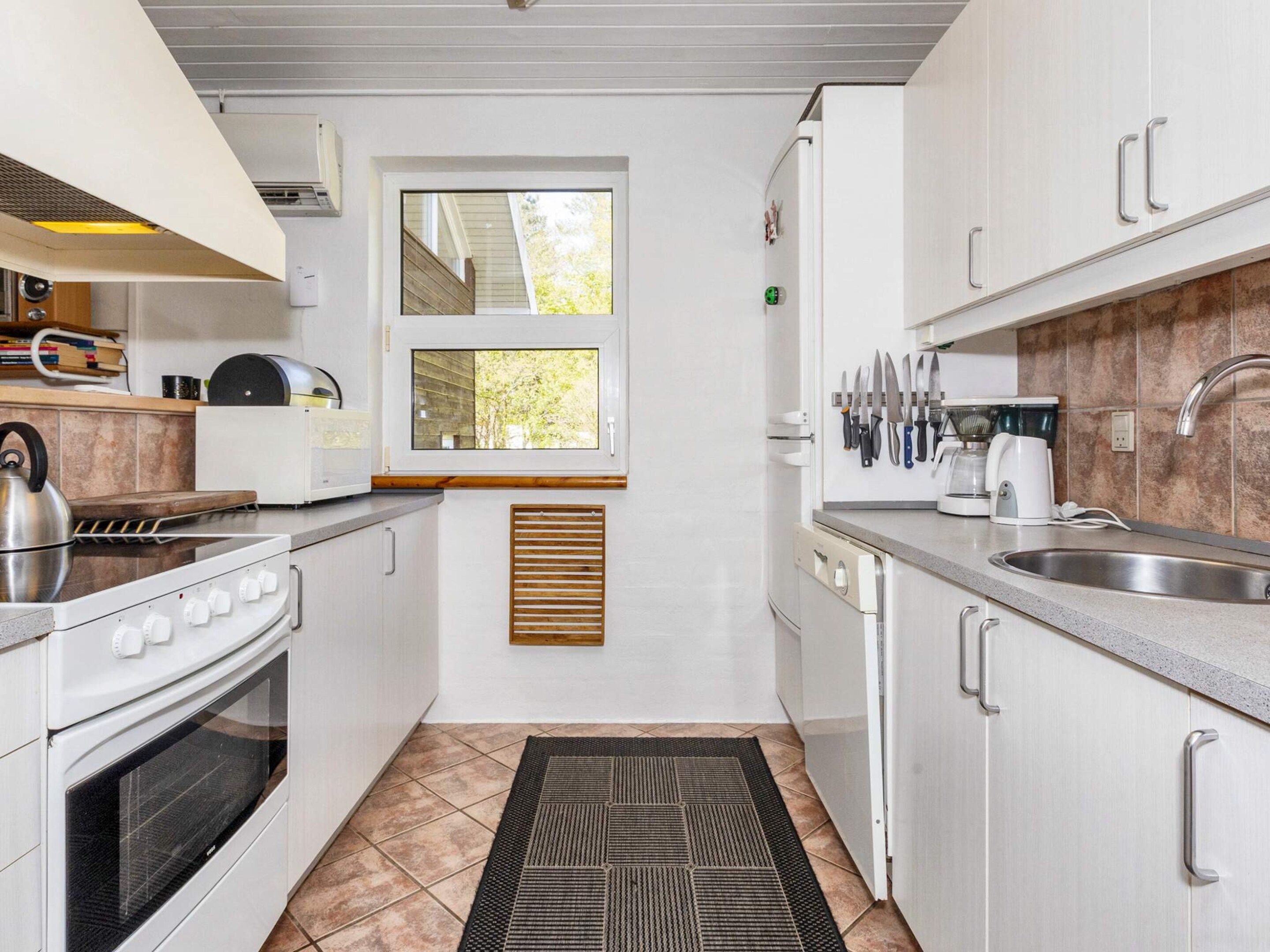 A modern kitchen with white cabinets, a stove, a window, and a sink.