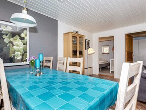 A dining area with a blue-tiled table, white chairs, and a wooden cabinet with glass doors.