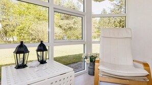 A room with large windows, a white chair, and two black lanterns on a white table. - 8 Person Holiday Home in Hojslev (Hojslev)