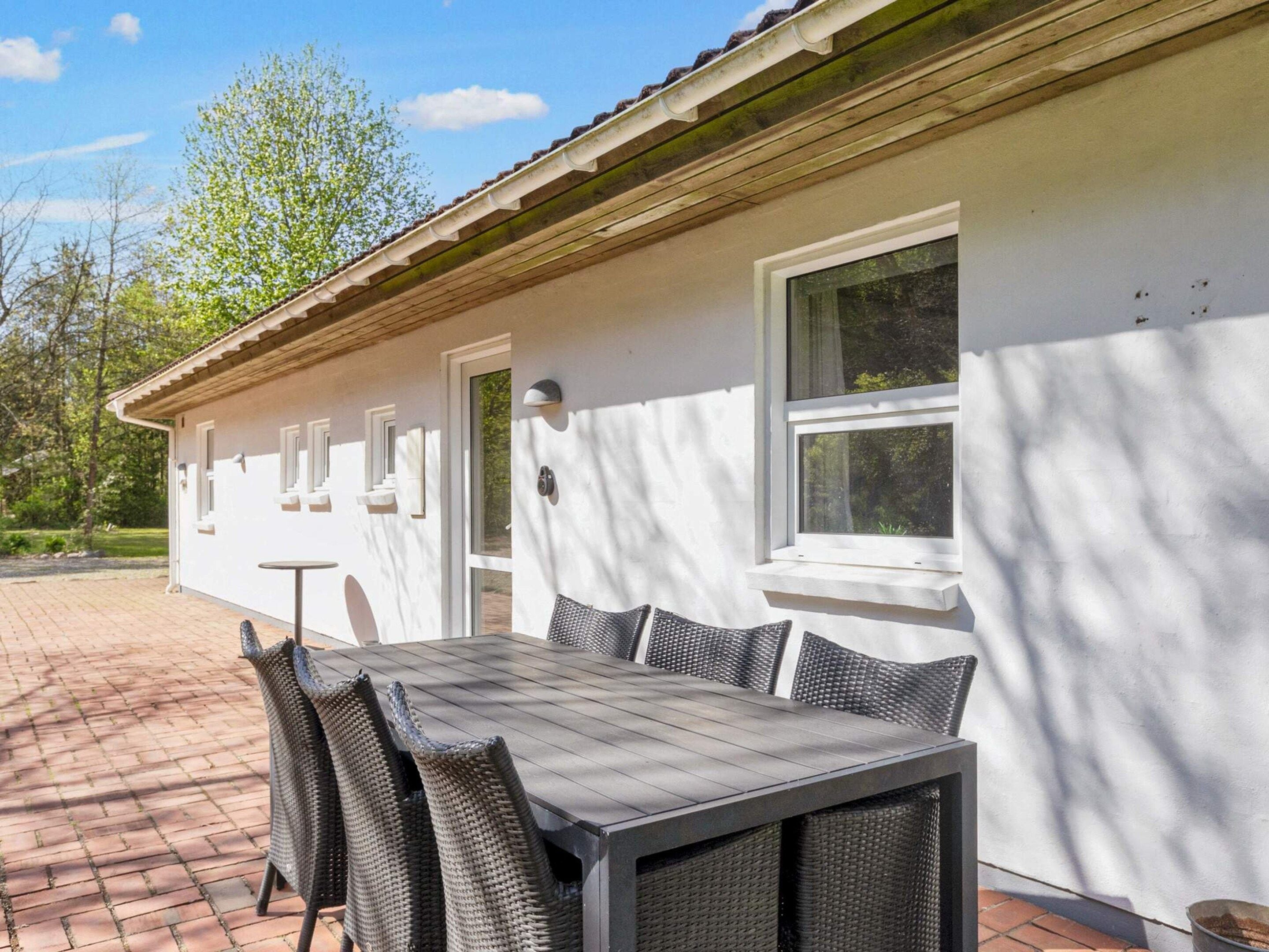 A patio with a table and chairs, a white building with windows, and a brick pathway.
