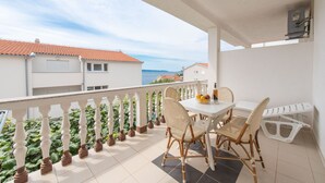 Un balcon avec une table et des chaises blanches, un petit banc blanc et une plante en pot.