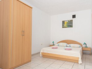 Een slaapkamer met een houten garderobe, een bed met een witte spreidek, twee nachtkastjes met lampen, en een schilderij aan de muur.