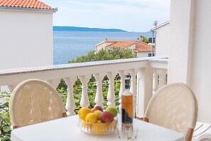 Een balkon met een tafel, stoelen, een schaal fruit en een fles.