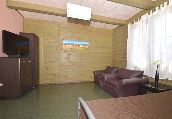 A room with a wooden wall, a television on a cabinet, a brown sofa, and a bed with a headboard. - Cozy Studio 3 at the Seaside Agrotourism (Darlowo)