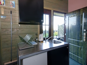 Kitchen area with a stainless steel countertop, wooden paneling, and a window offering a view of the surrounding greenery.