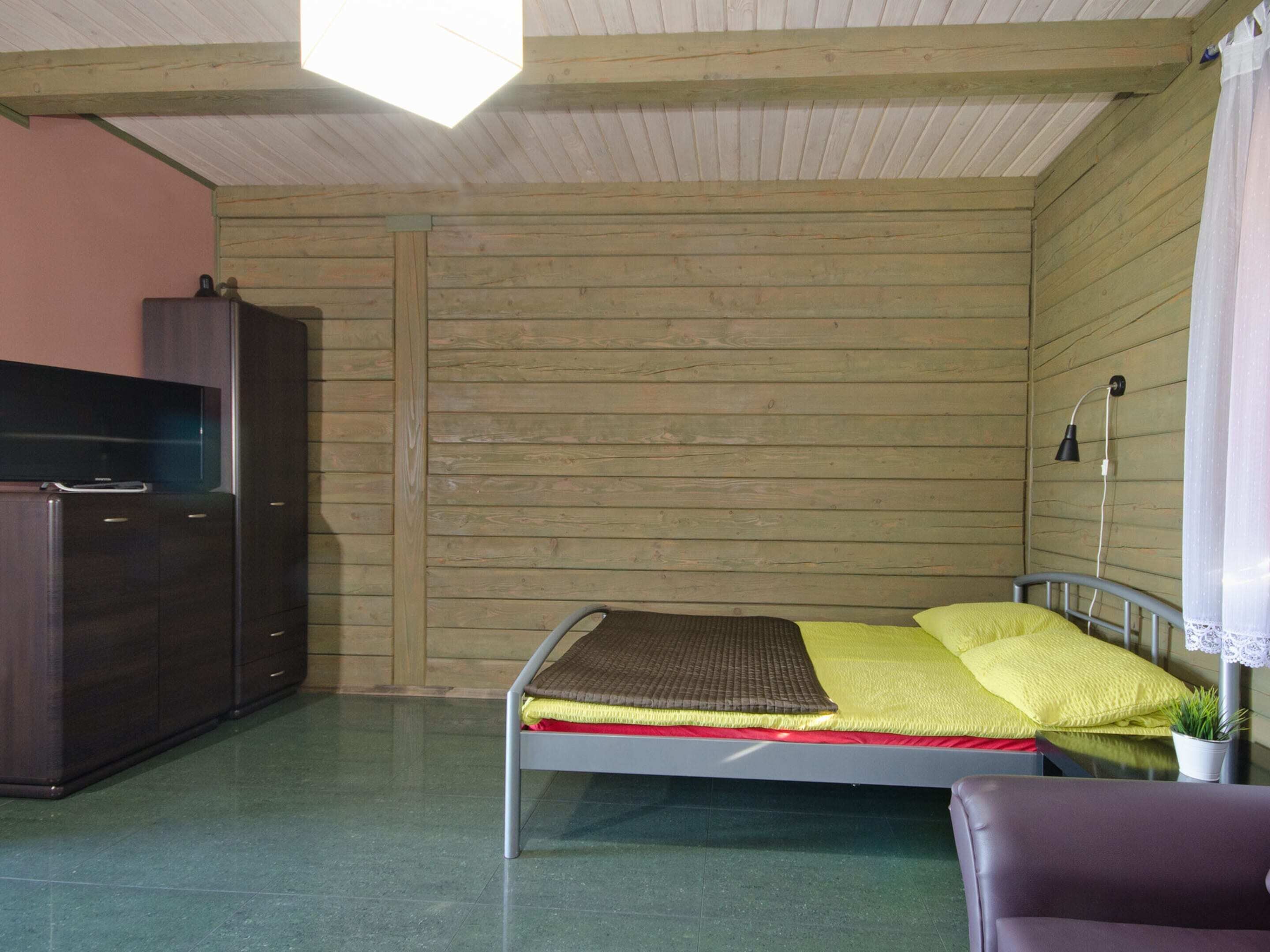A small, compact room with a bed, a wardrobe, a desk, and a lamp.