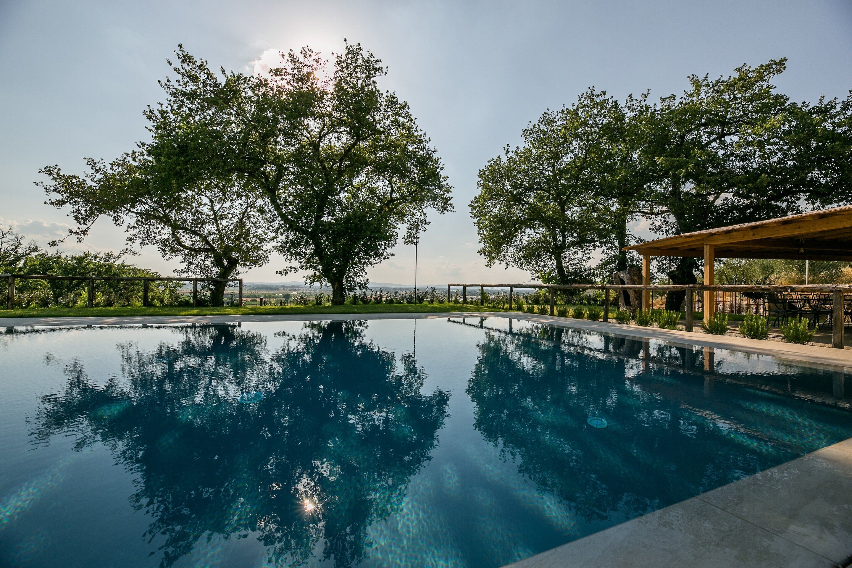 A clear view of a swimming pool with surrounding trees and a wooden pergola.