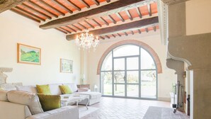 Un salón amplio con un sofá blanco, una araña y un gran ventanal de arco.