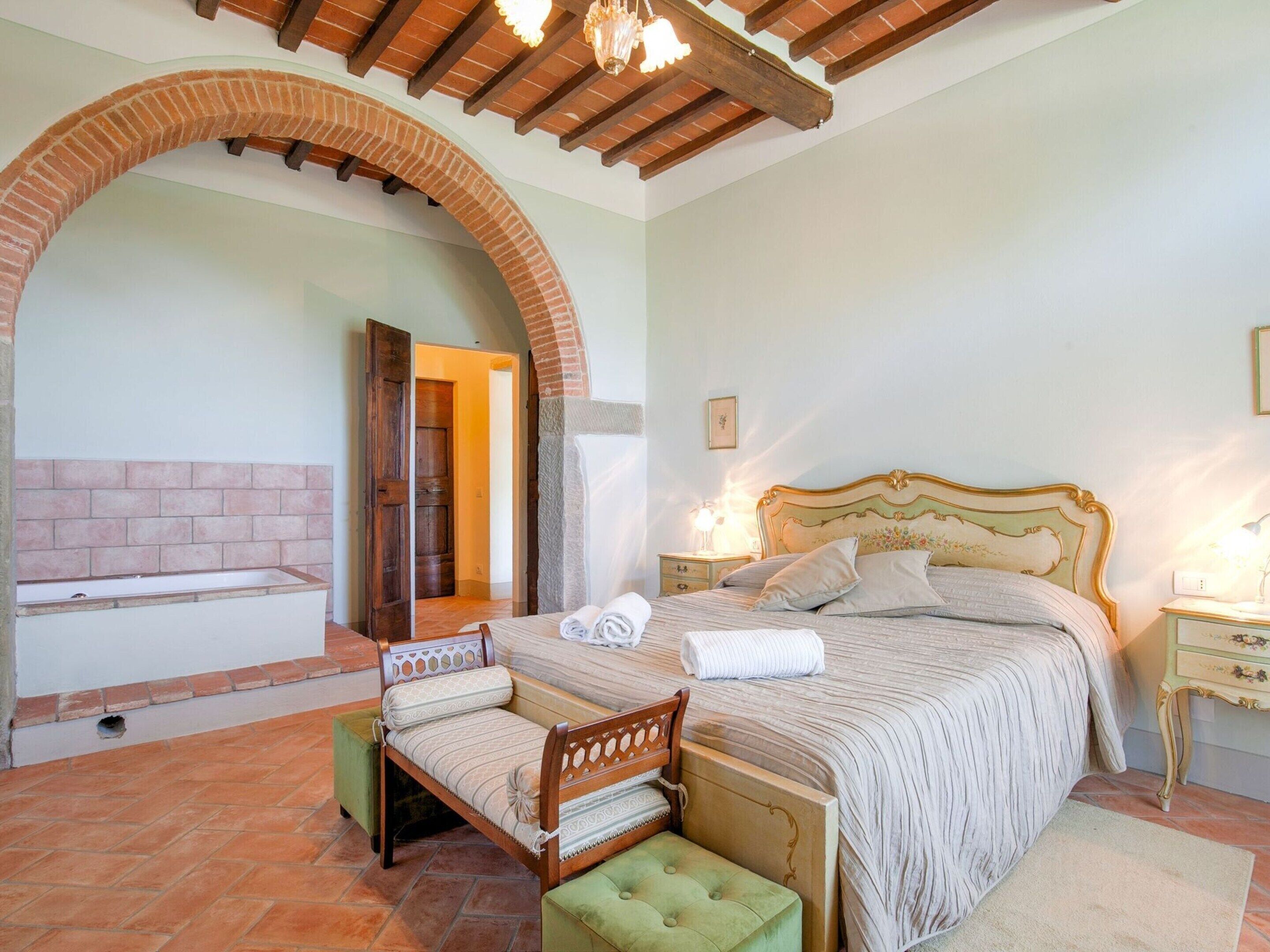 A bedroom with a large bed, a wooden bench, a small table, and a bench seat.