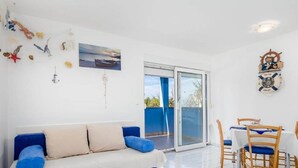 A modern living room with a blue sofa, a dining table with chairs, and a sliding glass door leading to an outdoor area. - Seaside Apartment in Mandre (Kolan)