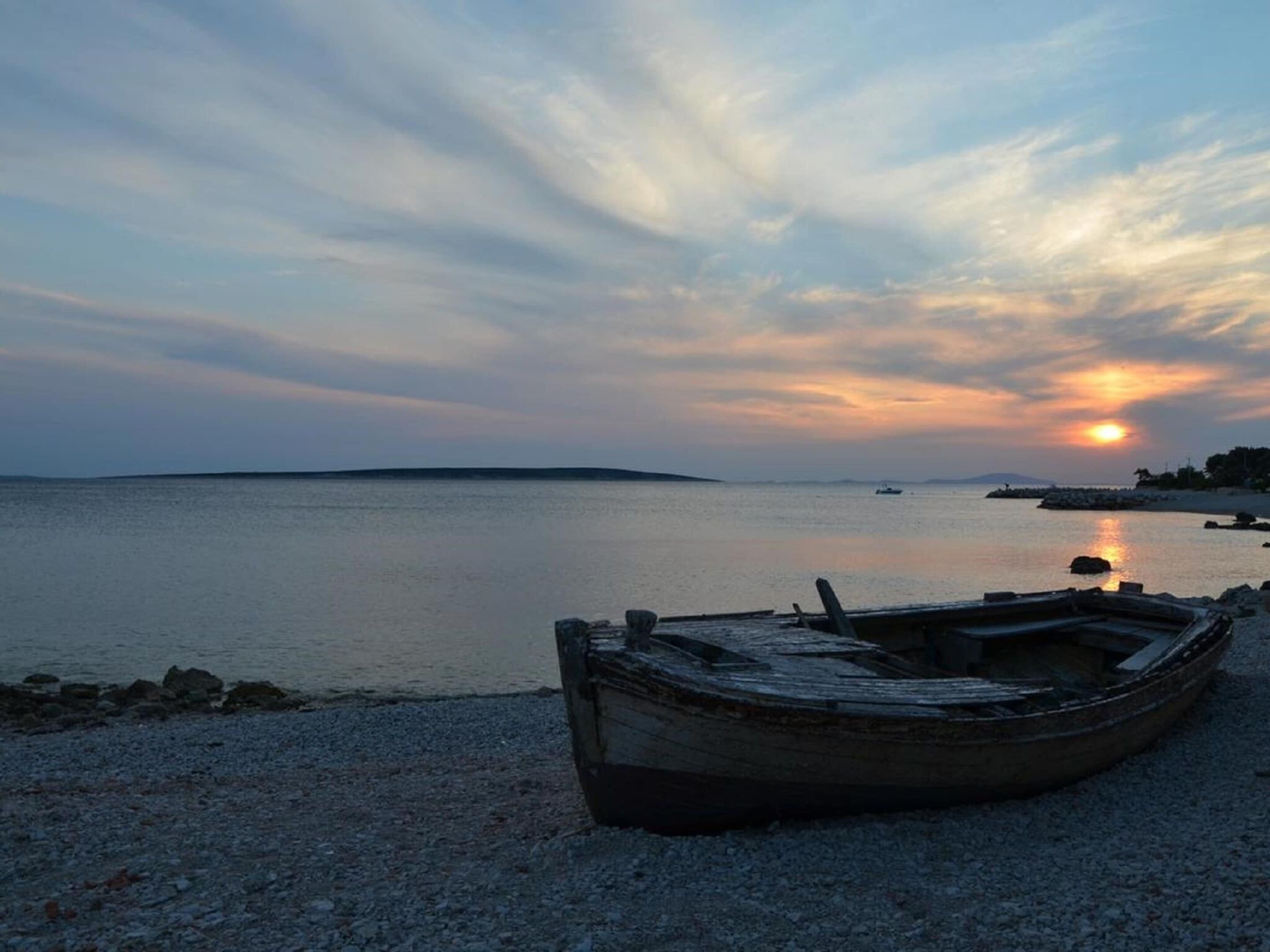 A boat on a pebbled shore with a sunset in the background.