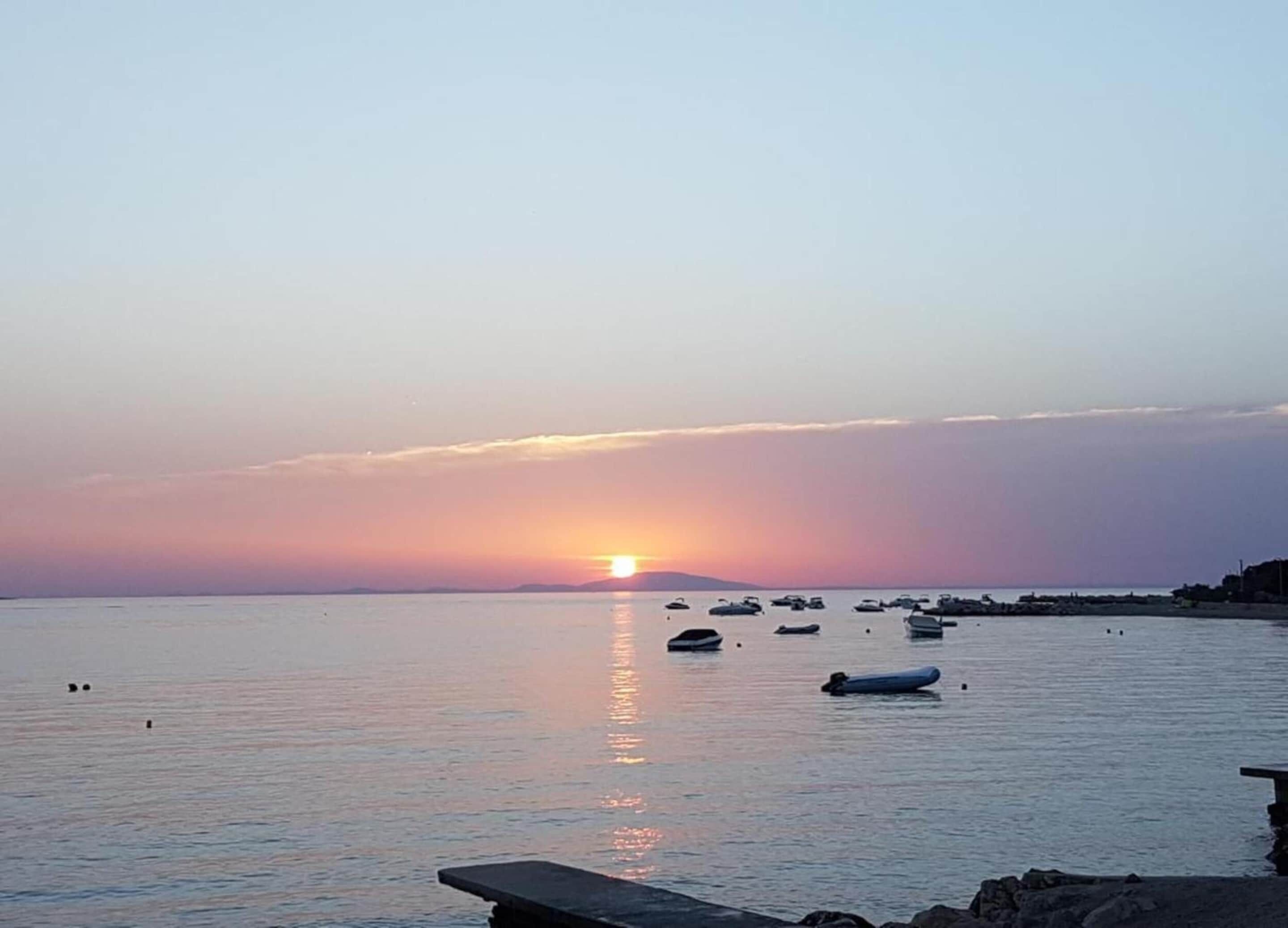 Mar tranquila al atardecer con barcos y un muelle.