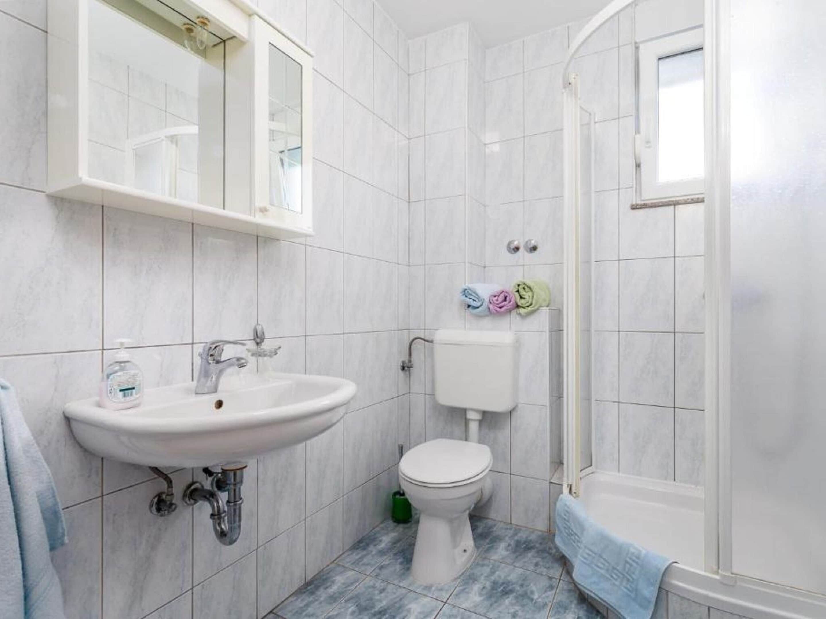 Une salle de bain avec un lavabo, des toilettes et une douche, le tout de couleur blanche.