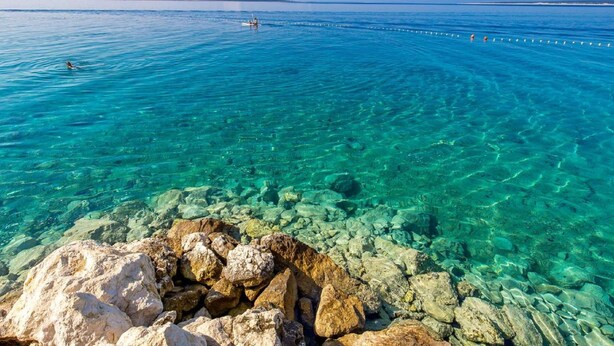 A clear view of a rocky shoreline with calm water, a distant boat, and a clear sky. - Mandre Coastal Hideaway (Kolan)